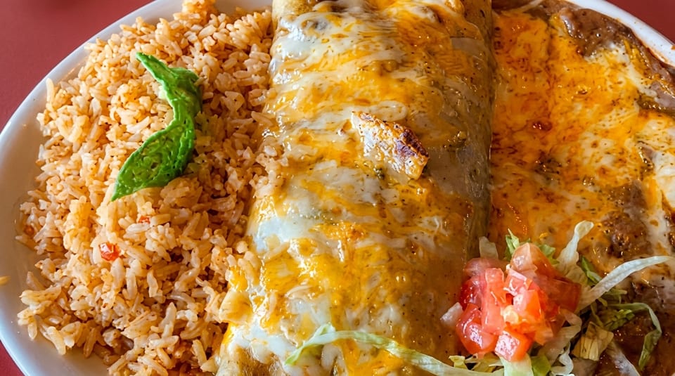 A close-up of a cheesy burrito, rice, and refried beans with lettuce and tomato.