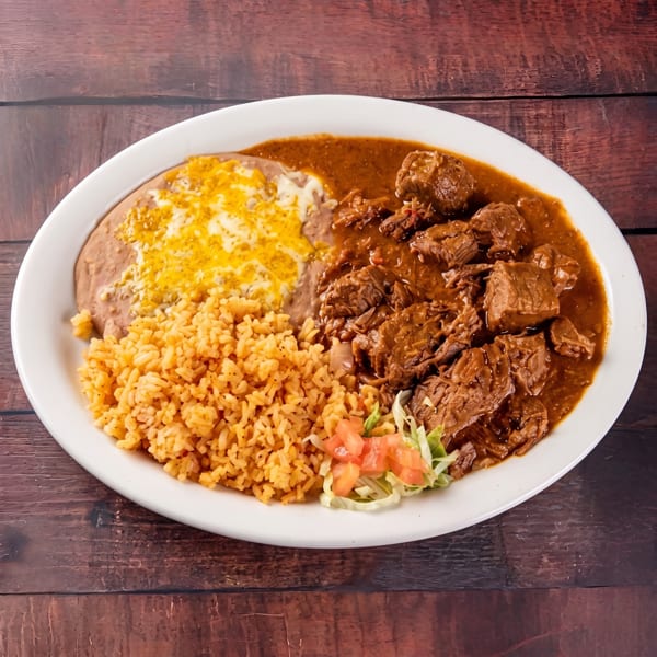 A white oval plate with carne guisada, rice, refried beans with cheese, and a small salad.